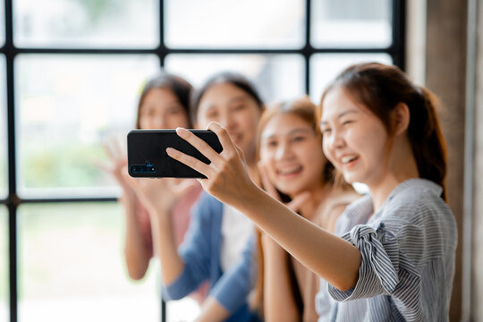 Beautiful Asian woman holding a mobile phone up to take pictures with a group of friends at work, taking pictures using a new smartphone. shooting concept selfie from a smart communication device.