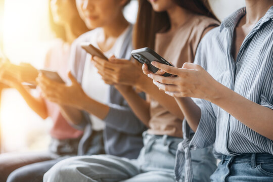 Groups of women sit in a row in the room, playing with cell phones. The concept of using a smartphone communication tool to play social media and send messages to talk to people through applications.