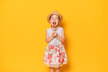Girl in dress licks watermelon-shaped lollipop against yellow background.
