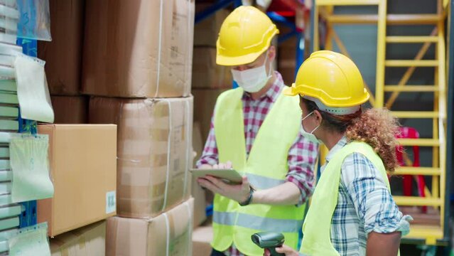 Two Warehouse Workers In Face Mask Doing A Stocktaking In Warehouse, With African Female Worker Shooting Barcode On Cardboard Box By Barcode Scanner While Caucasian Male Worker Record Data On Tablet.