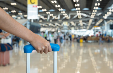 Woman hand holding baggage handle with blurred airport terminal background.