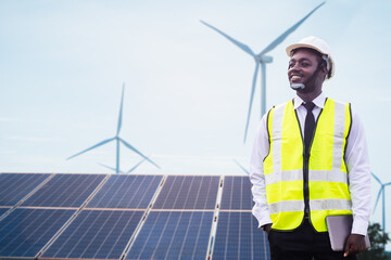 African engineer manager stand holding tablet front the solar photovoltaic and wind turbines...