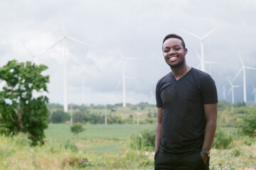 African man stands at a windmill that generates electricity and renewable energy for agriculture...