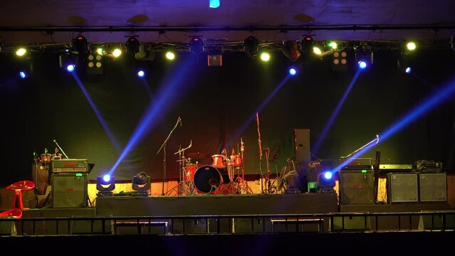 Front of the stage with band instruments, microphone stands, speakers while RGB LED and Moving LED stage lights are tested by moving,  shining with color-changing across the stage before show starts.
