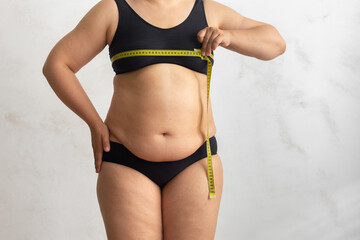 Unrecognizable naked overweight woman in underwear, hold and measuring by roulette tape her breast,...