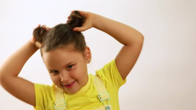 Little funny girl smiling with gap in mouth from fallen tooth, emotionally holding with hands buns of hair and leaning sideways closeup, white background. Concept of healthy teeth and beautiful smile.