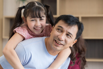 Happy child daughter sit on father back piggyback play at home. Smile dad hold little girl with arms carry on back. Family, Parents concept.