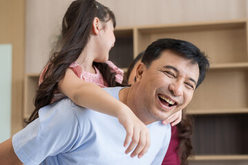 Happy child daughter sit on father back piggyback play at home. Smile dad hold little girl with arms carry on back. Family, Parents concept.