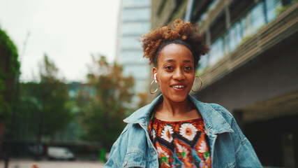 Fototapeta premium Closeup, сute African girl with ponytail, wearing denim jacket, in crop top with national pattern, standing at the bus stop and looking at the bus schedule.