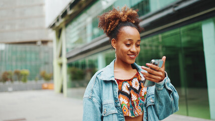Cute African girl with ponytail, wearing denim jacket, in crop top with national pattern, walking...