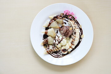 Roti cut into bite-sized pieces with banana and fried. Served with vanilla ice cream, whipped cream, sliced ​​almonds. and sliced ​​banana Topped with chocolate, decorated with pink flowers. 