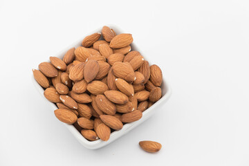 bowl with peeled almonds on a white background, one almond out of the bowl
