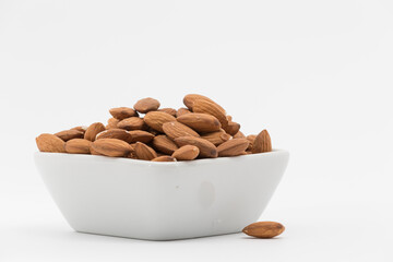 bowl with peeled almonds on a white background, one almond out of the bowl