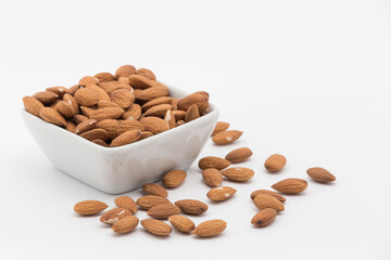 bowl with peeled almonds on a white background, one almond out of the bowl