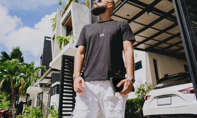 Young businessman walking out of his modern home with garage and car