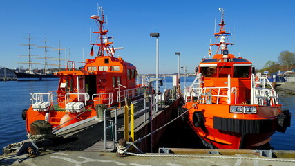 orange Lotsenboote warten an Hafeneinfahrt von Travemünde auf große Schiffe unter blauem Himmel