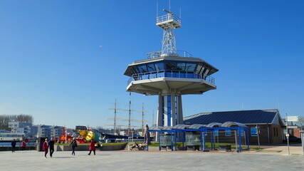 moderner Kontrollturm am Hafen von Travemünde mit Menschen auf der Promenade unter blauem Himmel