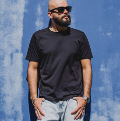 Male model with beard wearing black blank t-shirt on the background of an blue wall
