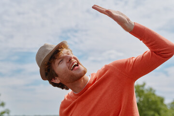 Handsome young redhead man in hat gesturing and smiling while standing outdoors