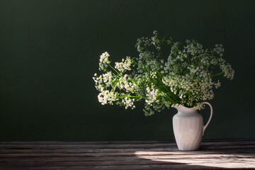 white wild flowers in jug on background green wall