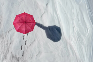 Top-down view of snow field with chain of footprints leading to man hidden under casting long shadow