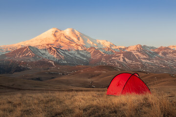 Golden light sunset with bright red tent in front of snow-covered Mount Elbrus, Caucasus, Russia © Igor