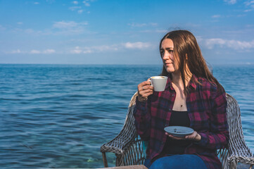 Young girl sitting in front of the sea with a cup of coffee
