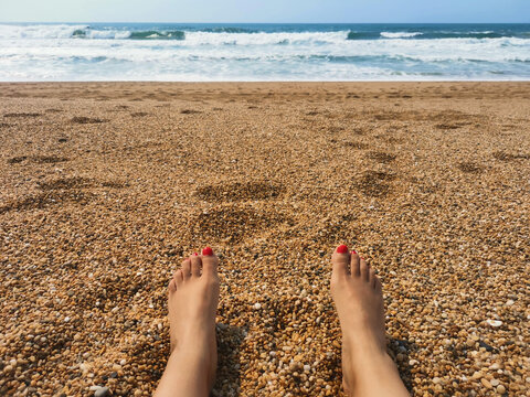 Pernas de jovem turista a relaxar sentada enquanto apanha banhos de sol na praia de areia sob o sol quente do ver&atilde;o