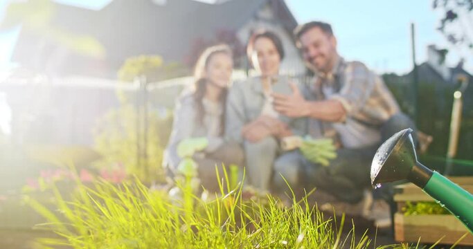 Happy Caucasian family with flowers in pots smiling to camera and taking selfie photo with smartphone. Working in orchard. Father, moher and daughter planting plants and making picture with phone.