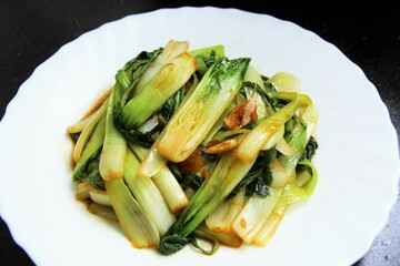 Cantonese vegetables stir fried with garlic and soy sauce on white plate. close up  photo isolate on black background top view