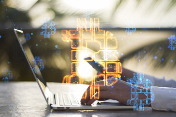 hands using laptop and cellphone with abstract glowing bitcoin sign hologram on desktop and blurry outside background. Cryptocurrency, finance, trade and market concept. Double exposure.