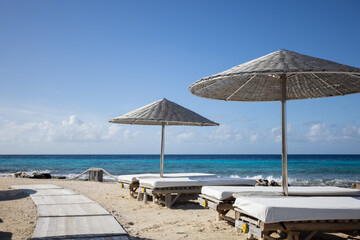 Fototapeta na wymiar Wooden sun loungers with sun umbrellas on a tropical beach.