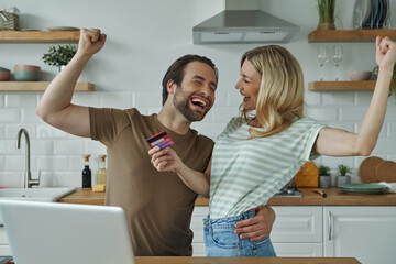 Cheerful young couple gesturing while shopping online from domestic kitchen