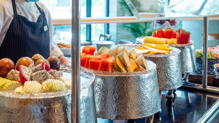 Fresh tropical fruits on buffet breakfast in hotel. A uniformed waiter stands at the food service...