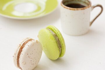 White and green macarons, cup of coffee on white background. Salted caramel macaroon, Pistachio nut macaroon. Close up