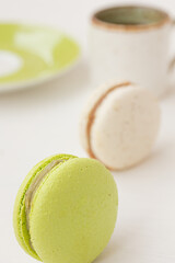 Green and white macarons, cup of coffee on white background. Salted caramel macaroon, Pistachio nut macaroon. Close up