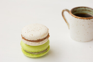 Green and white macarons, cup of coffee on white background. Salted caramel macaroon, Pistachio nut macaroon. Close up