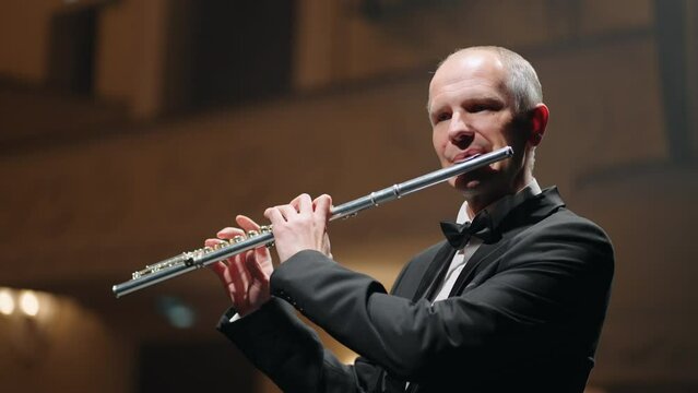 portrait of aged man with flute on scene of old music hall or opera house, talented musician is performing party