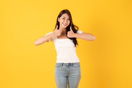 Smiling asian woman white shirt on yellow background with thumbs up show appreciate