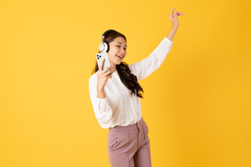 Smiling asian woman white shirt on yellow background using smartphone and wearing headphone listening music and dancing