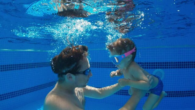 Father having fun with children in outdoor swimming pool into water, slow motion