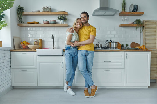 Full length of young couple embracing while standing at the domestic kitchen