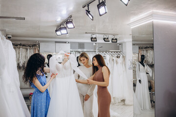 Bride with friends choosing wedding dress in boutique