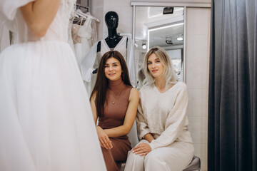 Obraz premium Woman helping bride wear wedding dress in boutique