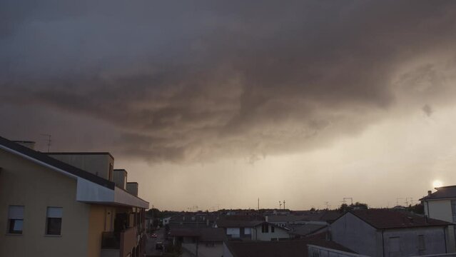 Huge storm passes over during sunset. Timelapse of a heavy rain-laden cloud mass under a yellow sky. Summer storms and climate change. Climate emergency. 4K quality.