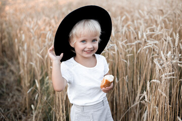 Beautiful portrait of a young child in a field. Children with bread. Little girl in cereal field. Happy baby girl on field of wheat with bread.