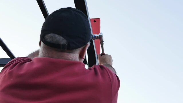 A strong powerful male assembler tightens by hand with a wrench a bolted connection of the steel structure of a training sports complex for sports. Installation of sports equipment