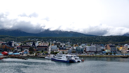 Fototapeta na wymiar Tour boats at the pier in Ushuaia, Argentina, with the town at the base of the mountains, shrouded by low hanging clouds, in the background