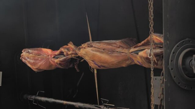 Process of cooking roasted whole ram carcasses on spit at summer outdoor food festival, market: close up, slow motion. Professional cooking, preparation, cookery, gastronomy and street food concept