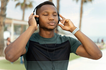 Man wearing headphones standing on the beach with closed eyes while listening music